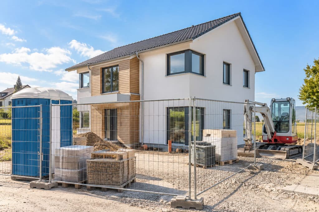 Baustelleneinrichtung mit Bauzaun, Material und Bagger vor einem Fertighaus